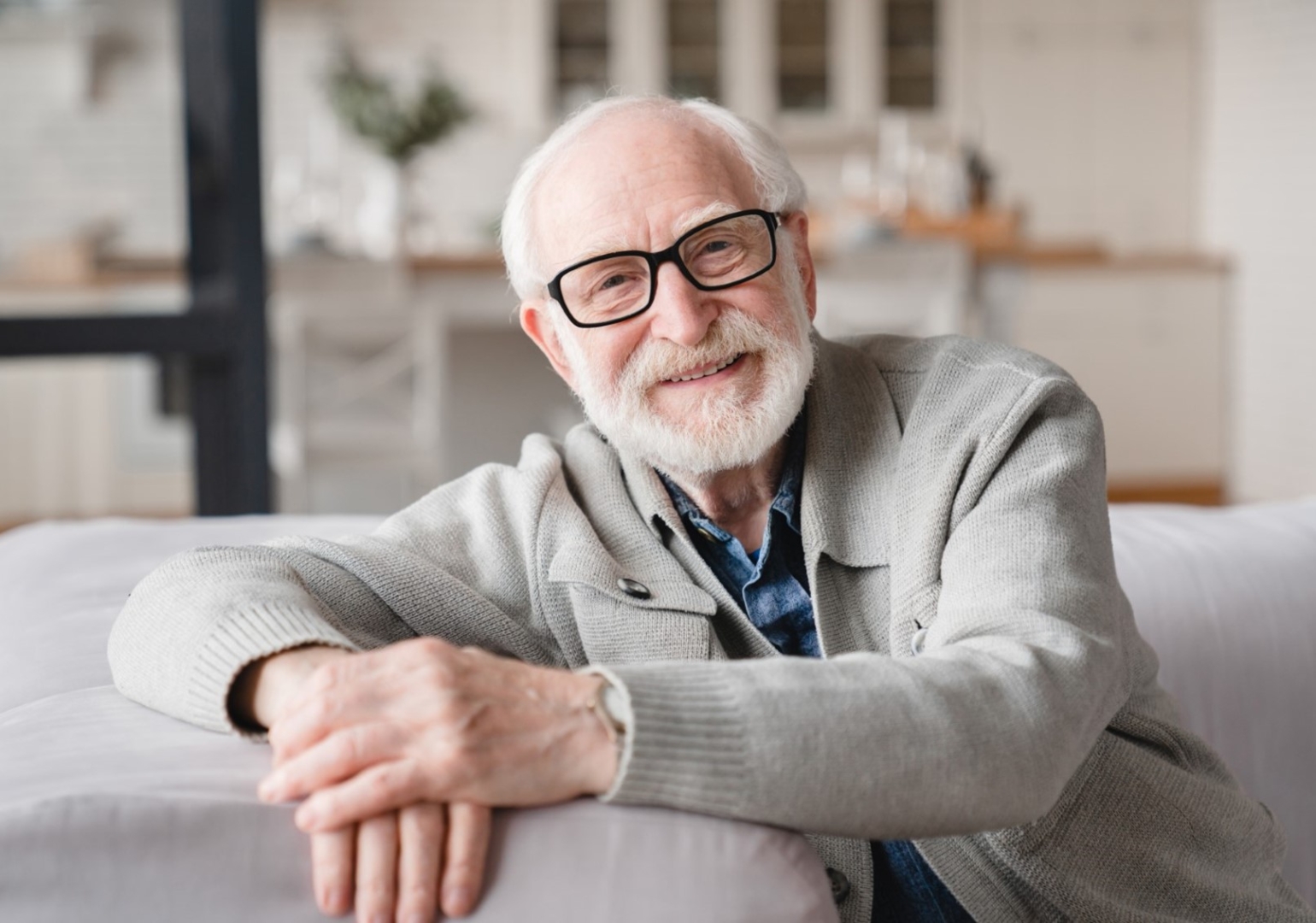 Elderly Caucasian man sitting on a couch smiling.